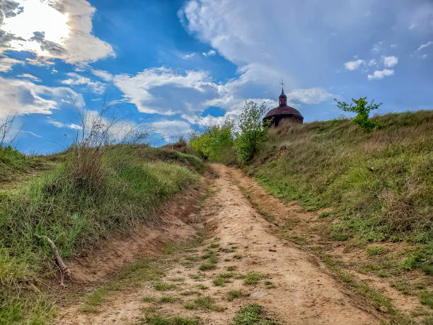 vista in basso di una piccola chiesa di legno o cappella su una collina contro un cielo blu. bellissimo paesaggio di campagna. sentiero battuto che porta - house wood dirt road footpath foto e immagini stock