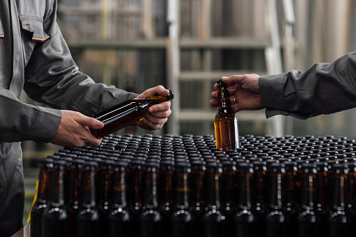 Lager Making Process: Unrecognizable Factory Workers Holding Bottled Beer
