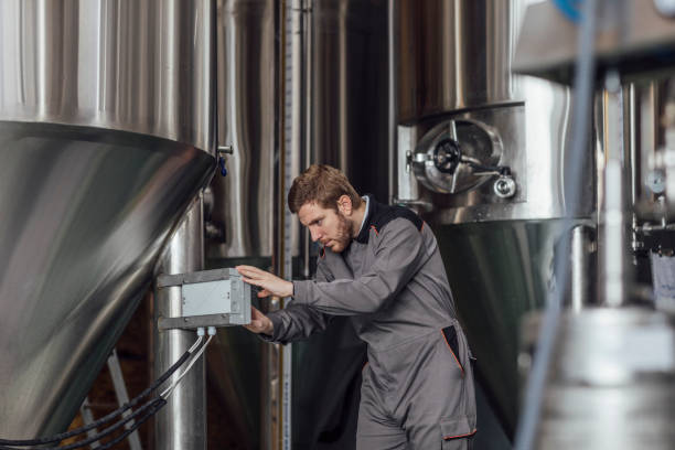 istock Quality Control at a Craft Brewery: Worker in a Uniform Checking the Beer Distillation Tanks 1222651892