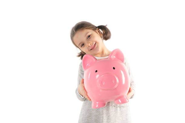 Toddler is holding big pink piggybank and is looking at camera with a toothy smile in front of pure white background.