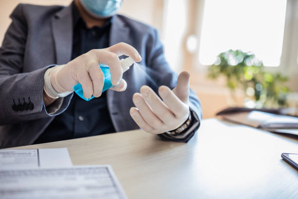 Business man disinfecting protective gloves Man wearing protective gloves at work and spraying disinfectant on them putting on latex gloves stock pictures, royalty-free photos & images