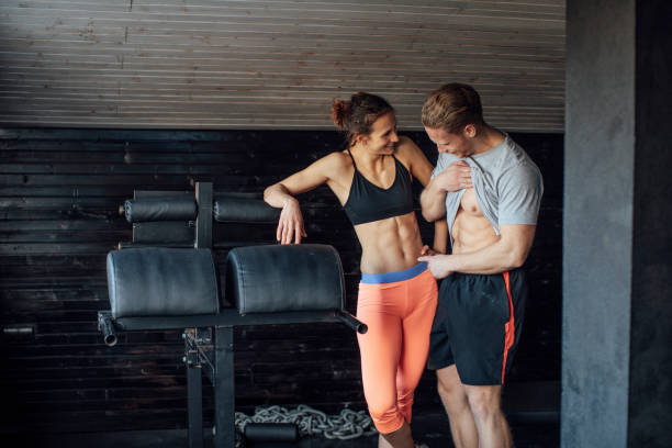 Checking the Progress: Muscular Man and Woman Looking at Each Other's Abs Showing off in the gym: sportsman and sportswoman checking out each other's six packs. fit woman showing off her muscular body and abs stock pictures, royalty-free photos & images