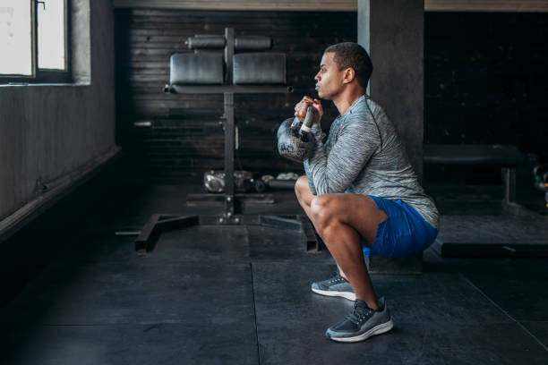 Sportsman Lifting Weights at a gym Gym Handsome serious African sportsman doing a squat with two kettlebells in his arms. Squats stock pictures, royalty-free photos & images