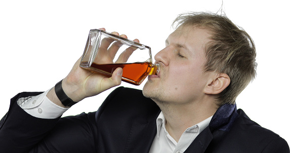 Portrait of sleepy young tired clerk man. Emotions. Depressed disheveled worker guy businessman in suit and white shirt drink alcohol cognac. White background. Office workaholic overworked concept