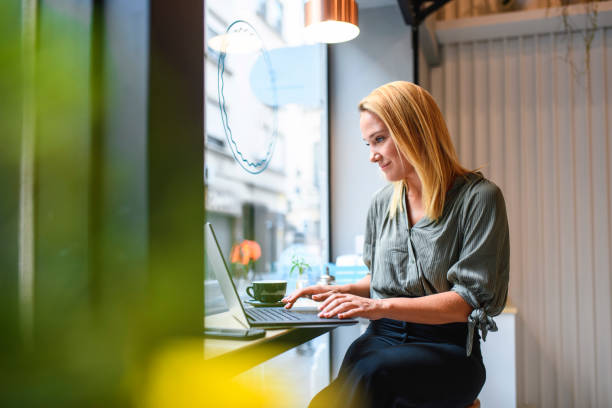 jovem empresária relaxada trabalhando em laptop no café - bars on windows - fotografias e filmes do acervo