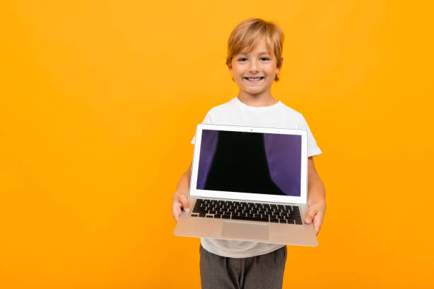 istock european boy holds laptop screen forward with mockup on yellow studio background with copy space 1222667978