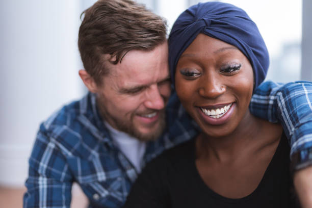 Husband hugging recovering wife A handsome caucasian man is hugging his stunning African American wife who is recovering from cancer. They are smiling and feeling optimistic. cancer illness stock pictures, royalty-free photos & images