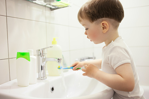 2 year old baby boy brushes his teeth with a toothbrush in the bathroom