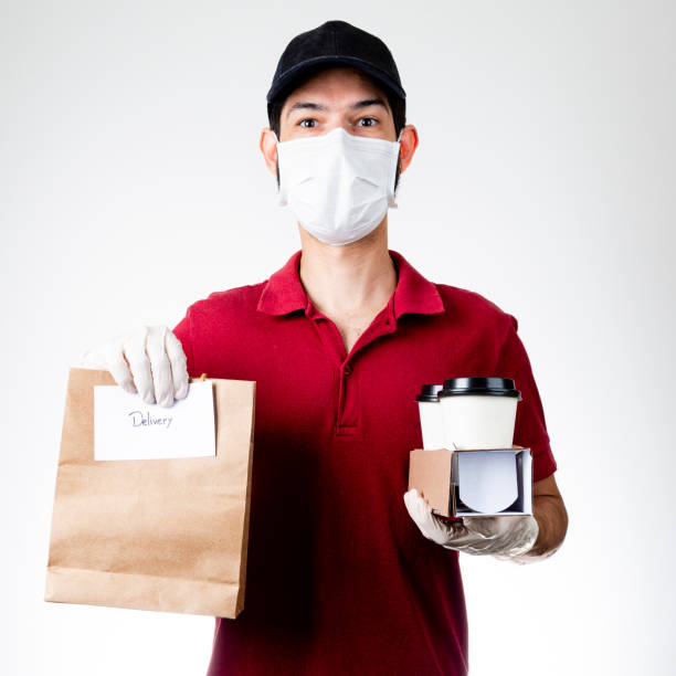 delivery man holding paper bag with food and drink on gray background, food delivery man in protective mask - restaurant food food and drink industry food service occupation imagens e fotografias de stock