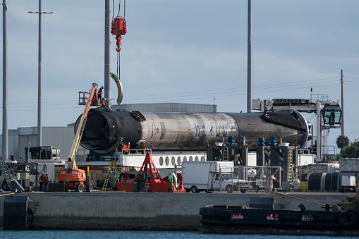 Cape Canaveral, FL, USA  - April 29, 2020: A SpaceX Falcon 9 rocket is supported by a crane and is being made ready for transport to a refurbishing facility. A lift supports workers on the rocket. This rocket was recovered at sea after launching on April 22 2020.