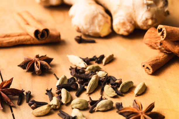 Closeup of chai spices ingredients, a fresh ginger root, star anises, whole cloves, cinnamon rolls and cardamom seeds on a rustic orange wood background
