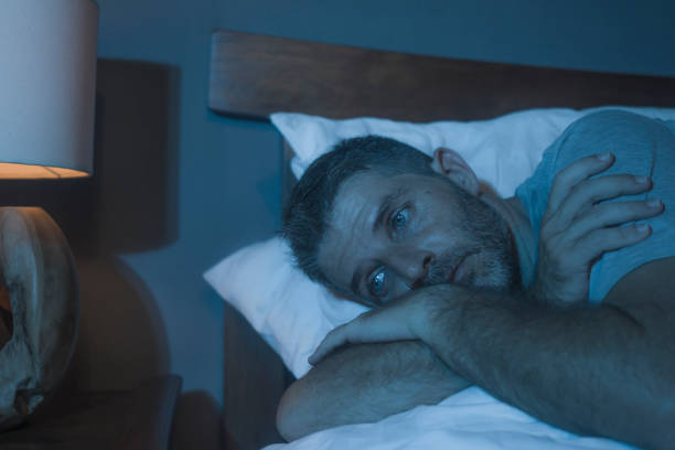 dramatic portrait in the dark of attractive depressed and worried man on bed suffering depression crisis and anxiety feeling lost lying sleepless in insomnia and life problem concept stock photo