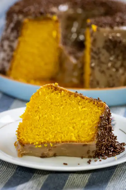 delicious piece of carrot cake with brigadeiro topping (chocolate cream and Brazilian milk candy), on a white plate with the cake in the background on top of a blue cloth