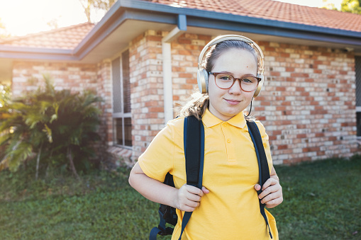 Young School Girl Wearing Headphones and Backpack Getting Ready for School In Front Of Residential House