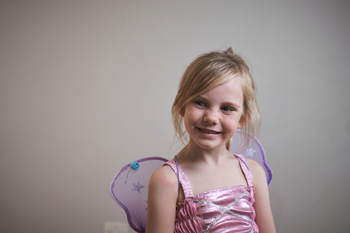 Close up portrait of a beautiful young girl in a pink fairy outfit. She is happy and smiling.
