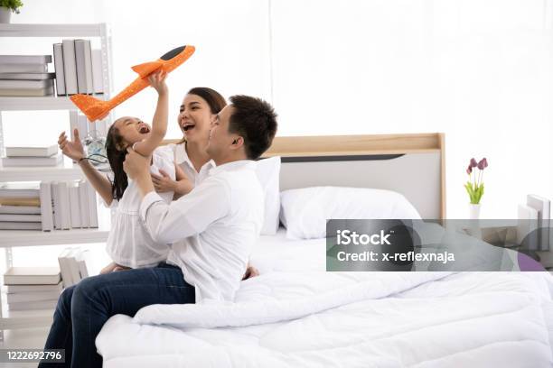 Asian Family Happy On The Bed In The House With Sunlight From The Window Father Mother And Daughter Aged Three Are Playing With A Plane Together Family Leisure Activities Stock Photo - Download Image Now