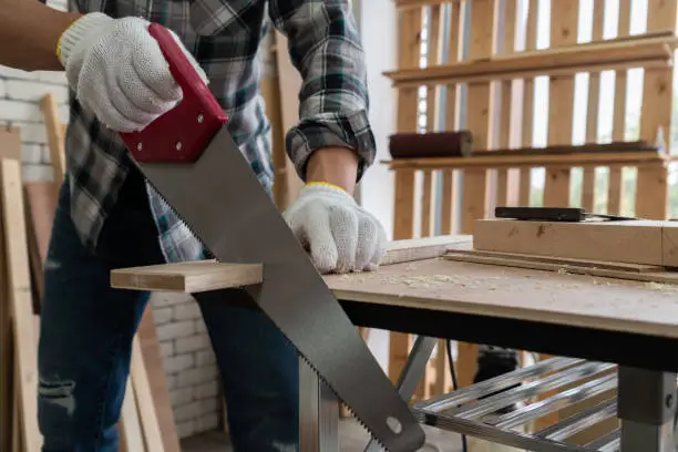 Carpenter working on wood craft at workshop to produce construction material or wooden furniture. The young Asian carpenter use professional tools for crafting. DIY maker and carpentry work concept.