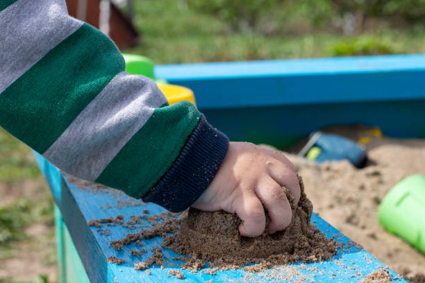 gioco di sabbia nella sandbox, mano di un bambino piccolo - playground cute baby blue foto e immagini stock