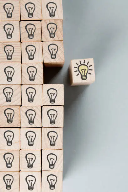 Wooden block group with dark and shining light bulbs imprinted. Shining one separated from the rest of the group. Idea, Innovation, Standing Out and Success Concept.