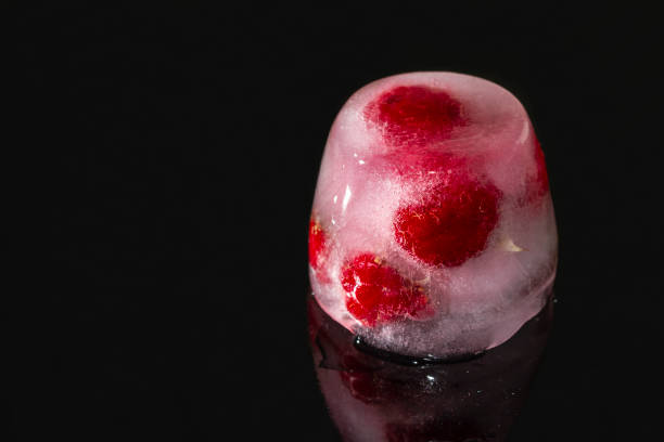 Raspberries frozen in ice blocks with reflection on dark background. Closeup, selective focus