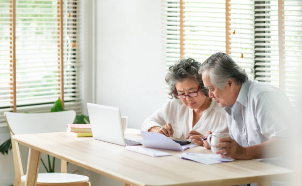 stressed asian senior couple mit taschenrechner und berechnen familienbudget, schulden, monatliche ausgaben zu hause während der finanzkrise. senior mann und frau blick auf kontobuch, rechnung, passbook, quittung und laptop-computer auf dem tisch - couple senior adult sadness emotional stress stock-fotos und bilder