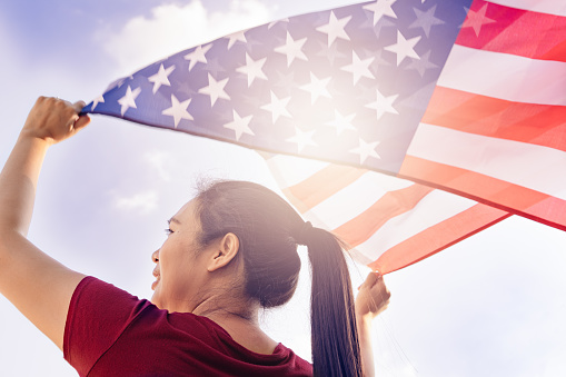 woman holding United States of America flag on sunny sky. USA Memorial day and Independence day concept.