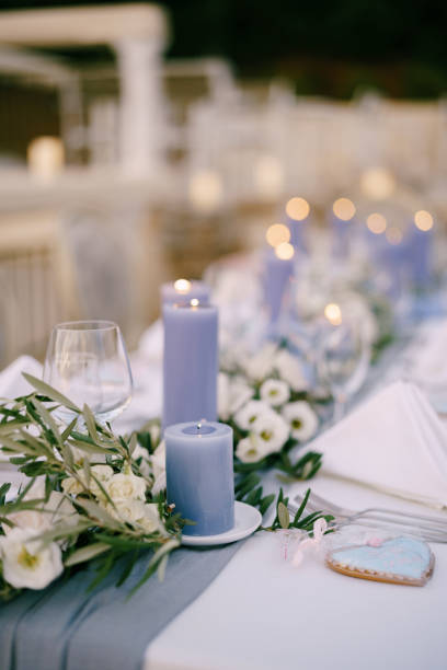 istock Close-up of a wedding dinner table at reception. Blue thick candles burn on the table among floral arrangements of white flowers and olive branches 1222718880