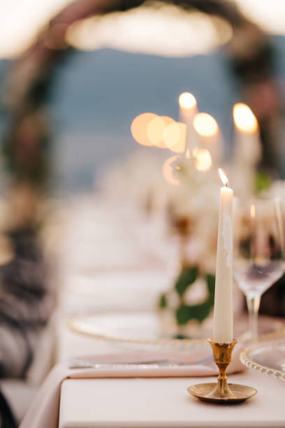 istock Close-up of a wedding dinner table at reception. A beautiful thin white candle burns in a small gold candlestick, frozen drops of wax dripping down. 1222721789