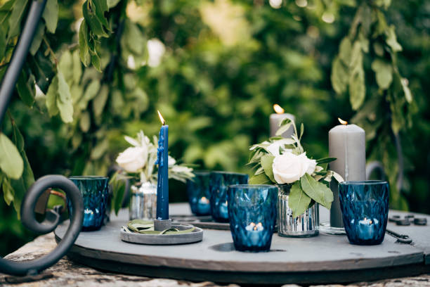 istock Close-up of a wedding dinner table at reception. Grey thick candles, blue thin candle, small tablet candles in blue glasses burn standing on a metal table on a green background. 1222722563