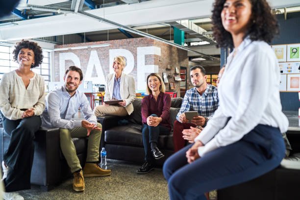 Happy multi-ethnic colleagues listening in meeting. Male and female business executives are sitting on sofa. They are planning in office.