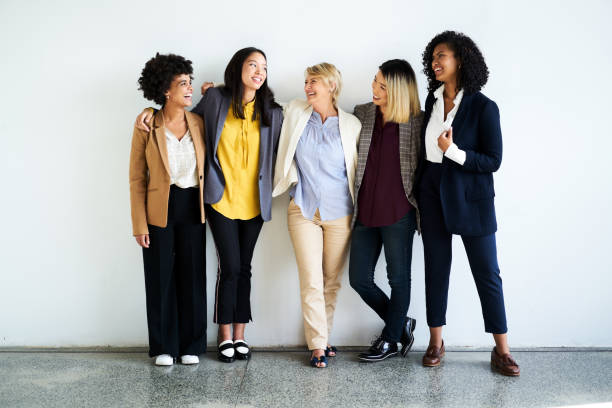 Happy female professionals talking at office Smiling multi-ethnic professionals standing against wall. Full length of happy female businesswomen in formals. They are at workplace. businesswomen group stock pictures, royalty-free photos & images