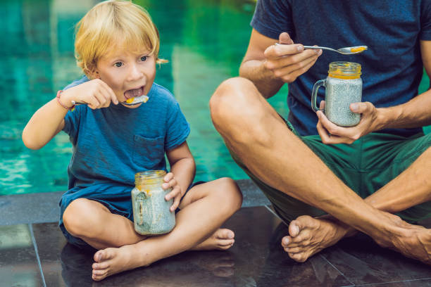 Father and son eat dessert with chia seeds and mangoes by the pool in the morning. healthy eating, vegetarian food, diet and people concept Father and son eat dessert with chia seeds and mangoes by the pool in the morning. healthy eating, vegetarian food, diet and people concept. eating chia seeds stock pictures, royalty-free photos & images