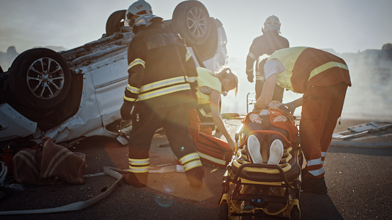 En la escena del accidente de tráfico: equipo de rescate de bomberos sacar a la víctima femenina de Rollover Vehículo, utilizan camillas con cuidado, entregarla a los paramédicos que realizan primeros auxilios photo