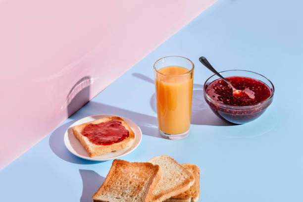 Breakfast with toast, jam and juice, lit by the sun on blue and pink backgrounds