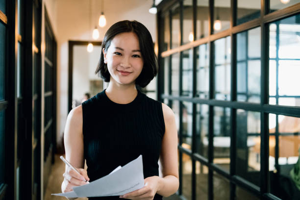 Cheerful businesswoman in her 30s with paperwork Waist up shot of beautiful professional woman smiling towards camera in office corridor, elegance, intelligence, working chinese woman stock pictures, royalty-free photos & images