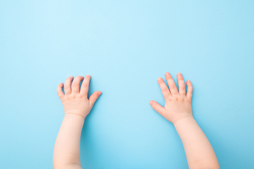 Two baby hands on light blue table background. Pastel color. Closeup. Point of view shot. Top down view.