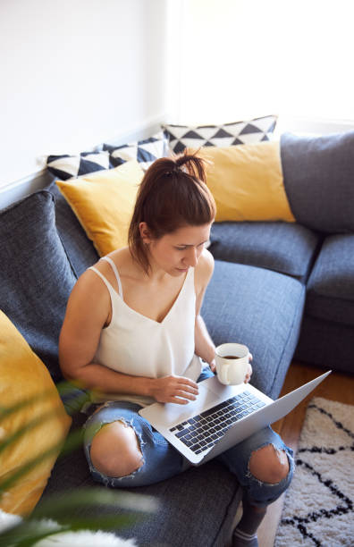 istock Smiling woman working on laptop sat on sofa drinking coffee 1222732511