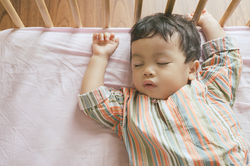 Little boy toddler adorably sleeping in his baby cot while wearing traditional Malay clothing, Ramadan and Eid concepts stock photo