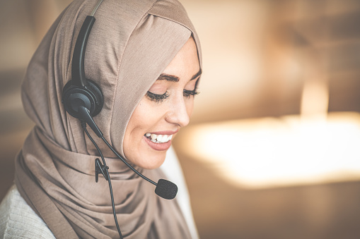 Muslim business woman with headset working in office. Happy arab woman working in company service center wearing headphone and using computer helping solving client problem