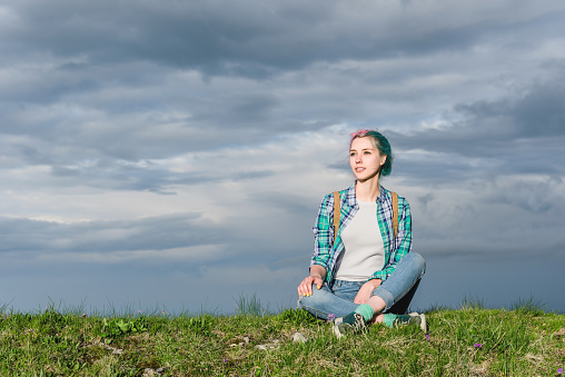 A beautiful girl sits on a field against the sky high in the mountains. The concept of relaxation and pastime.