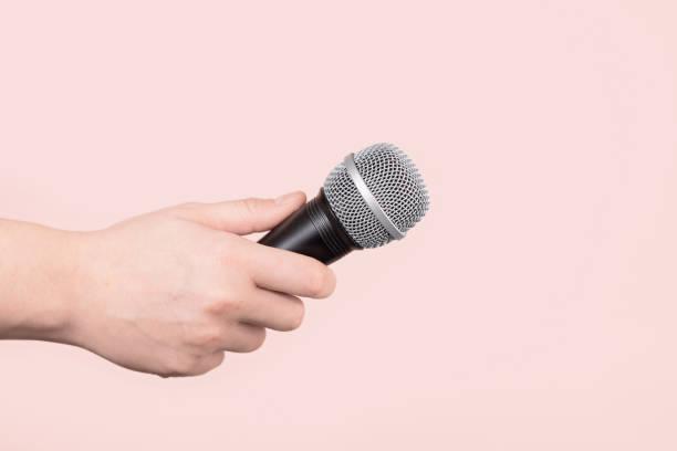 istock Hand holding up a microphone isolated against a pale pink background 1222739435