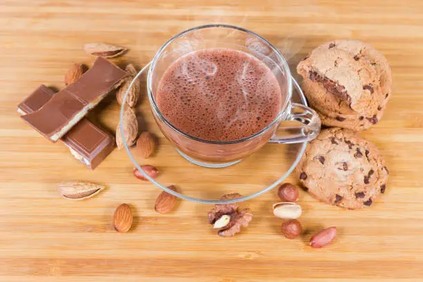 Photo of Hot chocolate among the nuts and confections on wooden surface