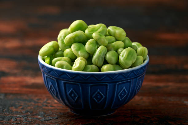 Green Broad Beans in a blue bowl on wooden table. healthy food Green Broad Beans in a blue bowl on wooden table. healthy food. fabes stock pictures, royalty-free photos & images