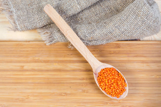 Uncooked red lentil in wooden spoon on wooden cutting board