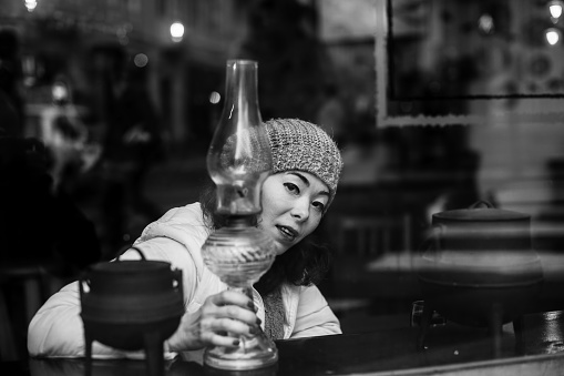 Multicultural asian woman looks out from behind the cafeteria window. Black and white photo.