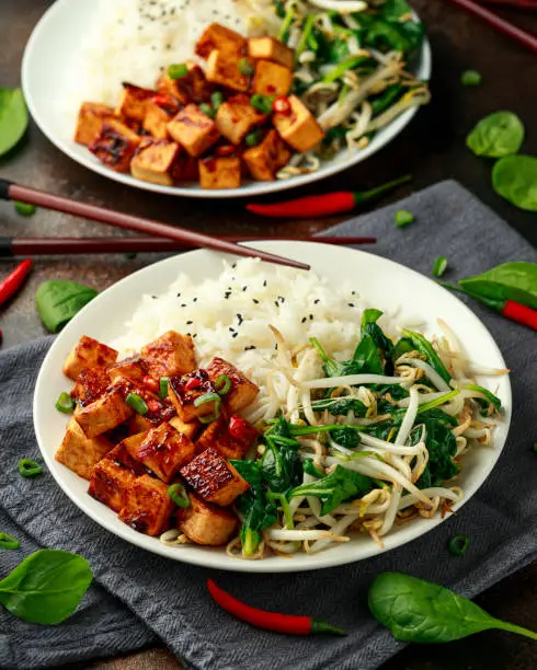 Fried Asian tofu in sweet chilli glaze served with rice, steamed spinach and beansprouts. Vegetable healthy food.