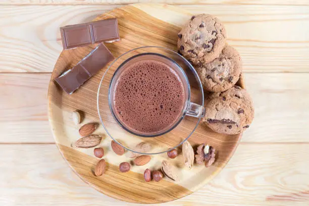 Photo of Hot chocolate, nuts and confections on wooden dish, top view