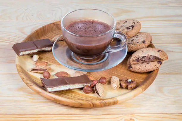 Photo of Hot chocolate among the nuts and confections on wooden dish