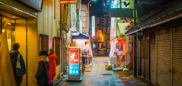 Hungry customers queuing outside a popular restaurant hidden down a quiet alleyway at night in the busy entertainment district of Dotonbori in the heart of Osaka, Japan’s vibrant second city.