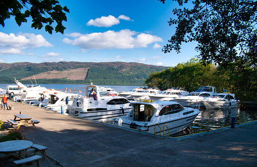 The pleasure hire boats of tourists on holiday moored at Urquhart Bay Harbour on Loch Ness in the Great Glen, Scotland, UK - taken on a sunny day with white clouds